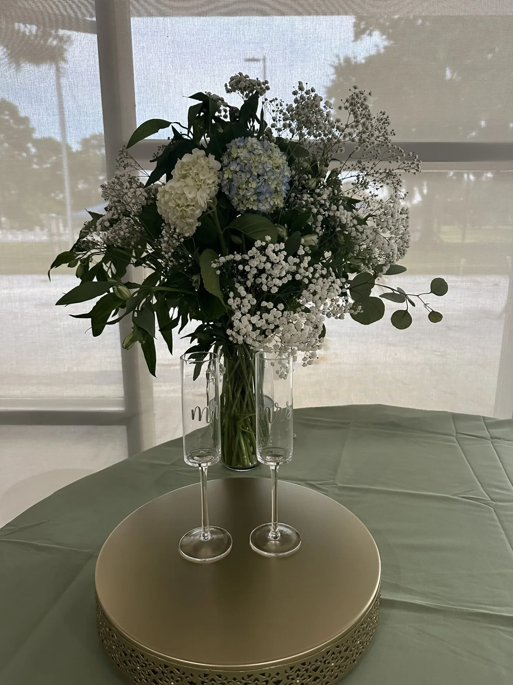Wedding centerpiece with hydrangeas, roses, greenery, and champagne flutes